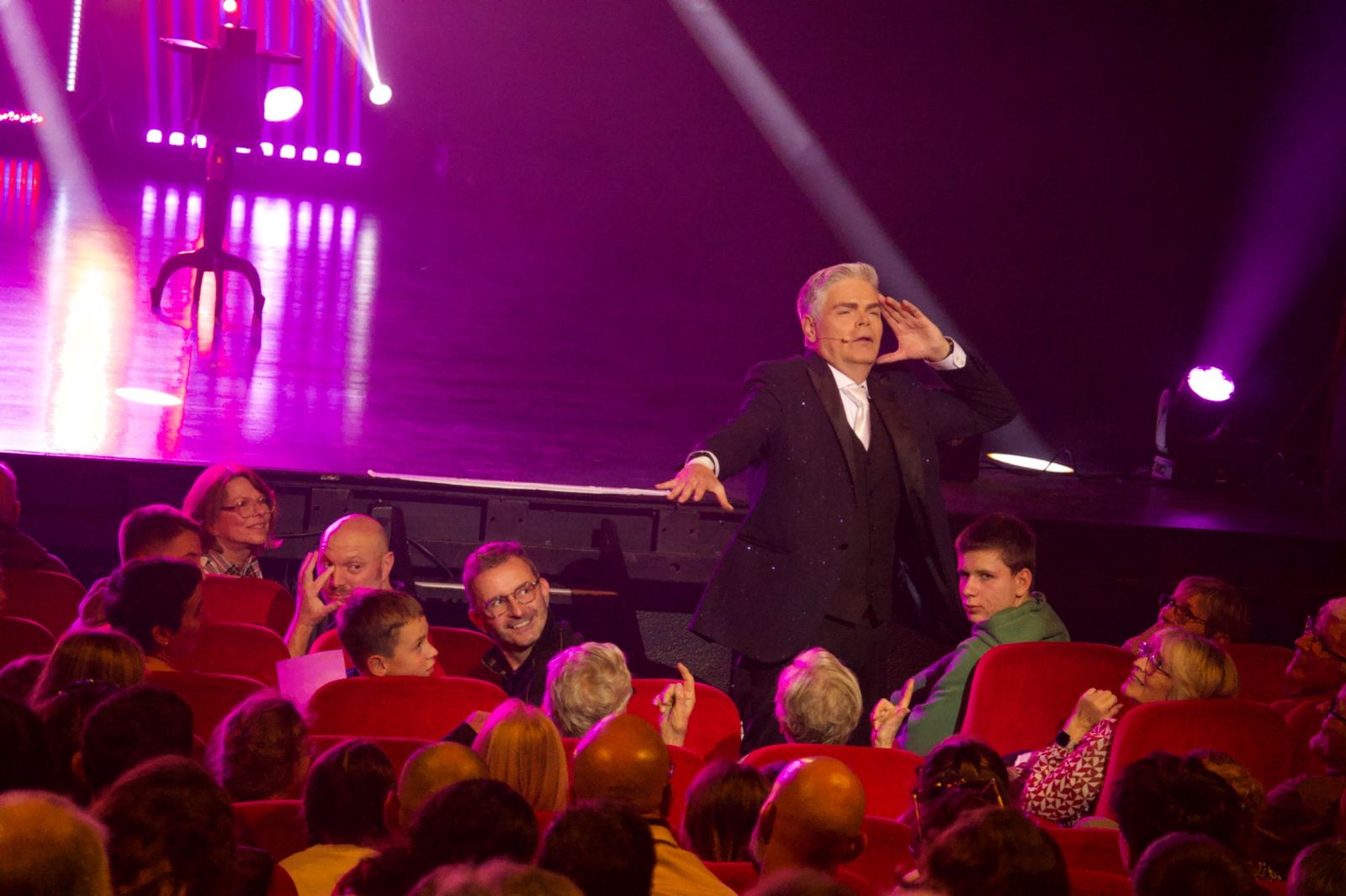 Nikola interagit avec le public dans une salle aux fauteuils rouges